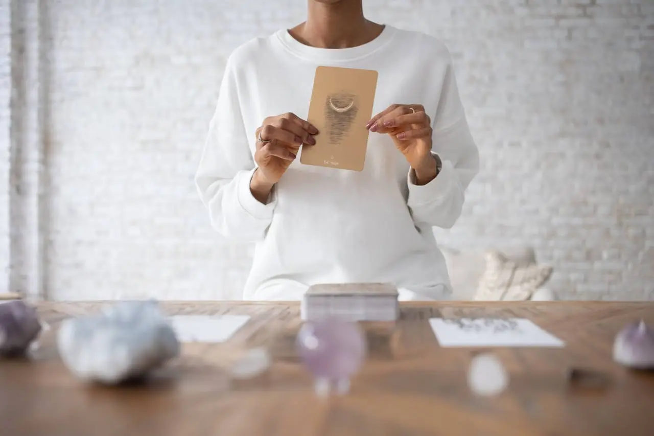 oracle-ou-tarot-quelle-difference Personne tenant une carte d’oracle lors d’un tirage divinatoire, ambiance douce et épurée